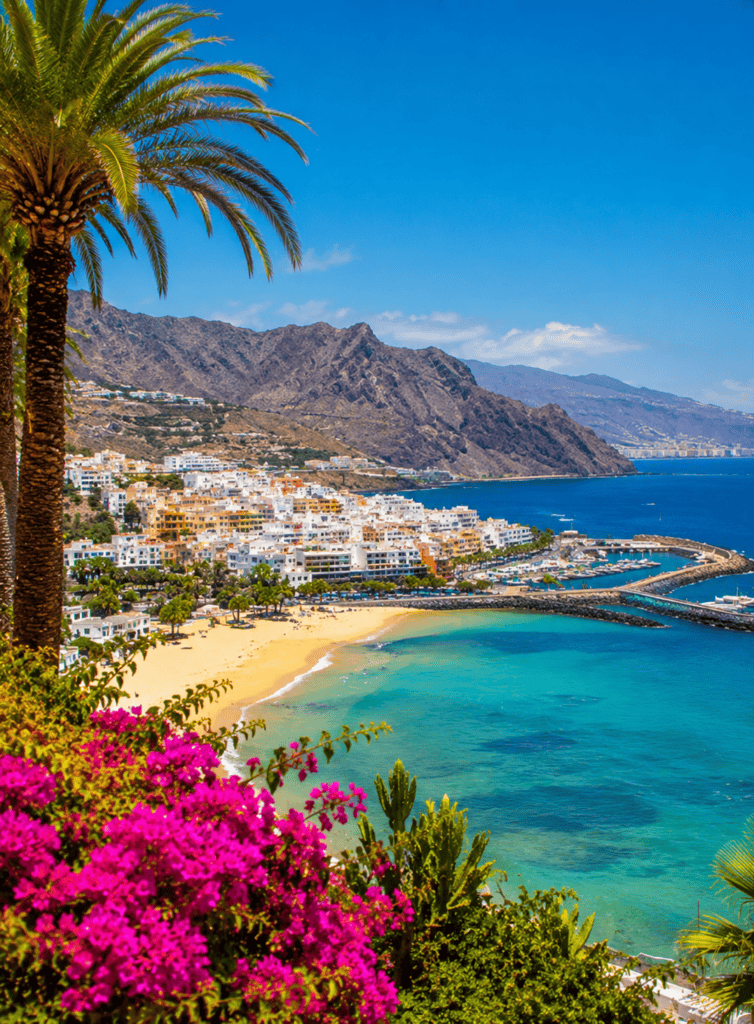 Beautiful Tenerife coast with colorful flowers, sandy beach, and mountain backdrop.